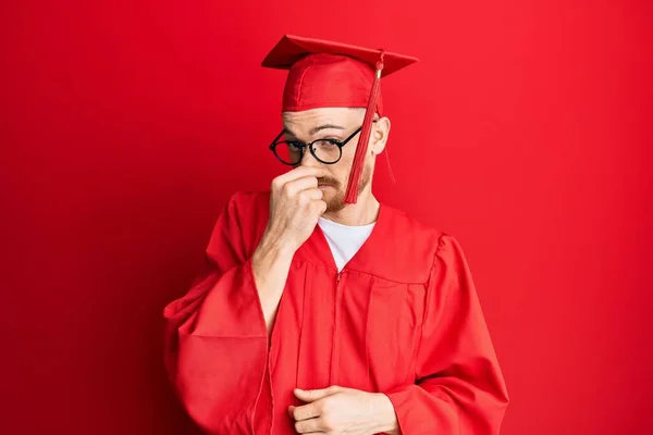 Young Redhead Man Wearing Red Graduation Cap Ceremony Robe Smelling — Stock Photo, Image