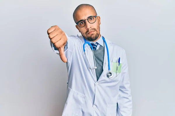 医者の制服を着たヒスパニック系成人男性と 親指を下にジェスチャーで拒絶と否定を示す不満と怒りを見て聴診器 悪い表現 — ストック写真