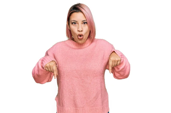 ヒスパニック女性とともにピンクの髪身に着けていますカジュアル冬のセーターPointingダウンとともに指ショー広告 驚きの顔とオープン口 — ストック写真