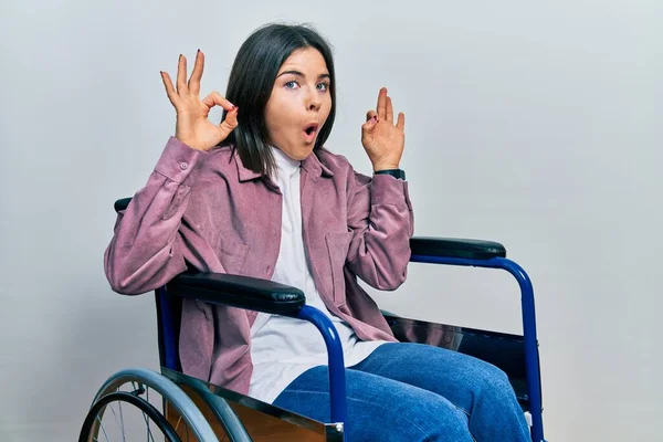 Jovem Morena Sentada Cadeira Rodas Parecendo Surpreso Chocado Fazendo Símbolo — Fotografia de Stock