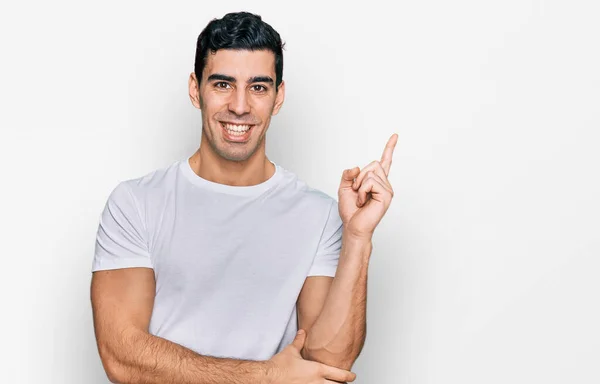 カメラを見ている側に手と指で指して 顔に大きな笑顔でカジュアルな白いTシャツを着てハンサムなヒスパニック系の男 — ストック写真