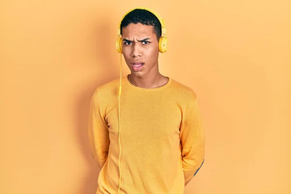 年轻的非洲裔美国人 用耳机在震惊的脸上听着音乐 面带怀疑和讽刺的表情 张开嘴让人吃惊 — 图库照片