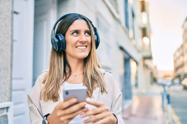 若い白人女性は 市内でスマートフォンやヘッドフォンを使用して幸せな笑顔 — ストック写真