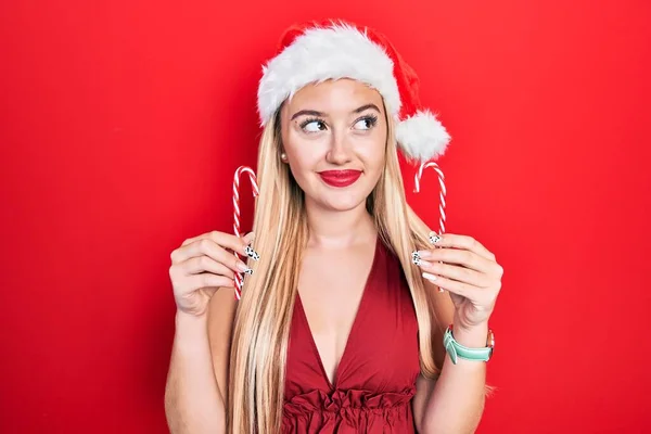 Jovem Loira Vestindo Chapéu Natal Segurando Doces Sorrindo Olhando Para — Fotografia de Stock