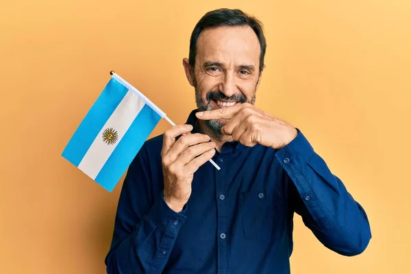 Hombre Hispano Mediana Edad Sosteniendo Bandera Argentina Sonriendo Feliz Señalando —  Fotos de Stock