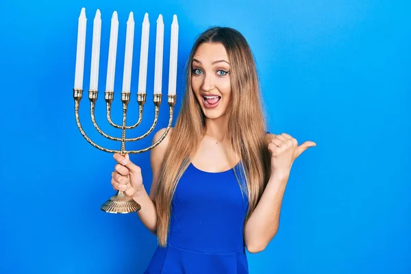 Young Blonde Girl Holding Menorah Hanukkah Jewish Candle Pointing Thumb — Stock Photo, Image