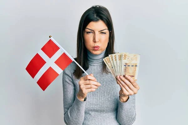 年轻的惊慌失措的女人举着丹麦国旗和克朗钞票 脸上带着滑稽的表情 气喘吁吁的 嘴被空气吹胀 — 图库照片