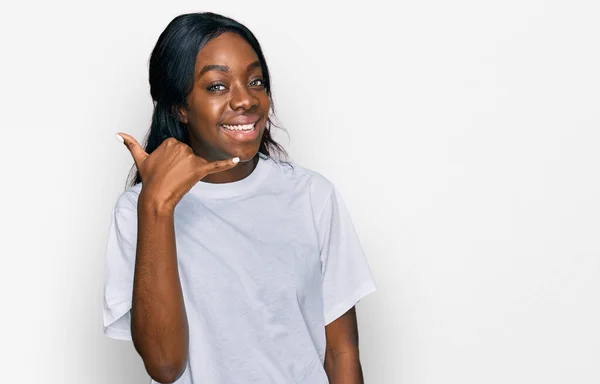 若いアフリカ系アメリカ人女性が白いTシャツを着て 電話で話すような手や指で携帯電話のジェスチャーをして笑っています コミュニケーションの概念 — ストック写真