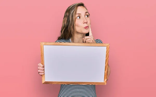 Young Blonde Woman Holding Empty White Board Serious Face Thinking — Stock Photo, Image