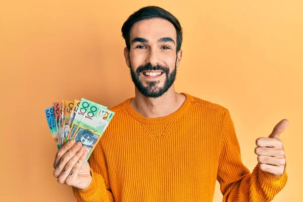 Joven Hombre Hispano Sosteniendo Dólares Australianos Sonriendo Feliz Positivo Pulgar —  Fotos de Stock