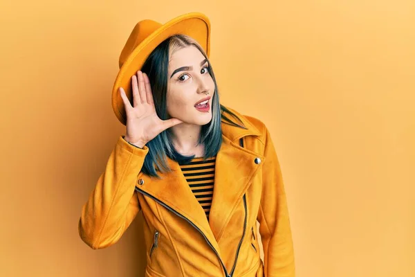 噂やゴシップに耳を傾ける耳の上に手で笑みを浮かべて黄色の帽子と革のジャケットを身に着けている若い現代の女の子 聴覚障害の概念 — ストック写真