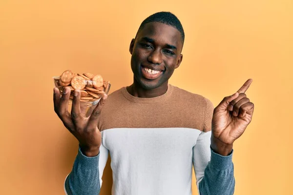 Joven Hombre Afroamericano Sosteniendo Tazón Con Galletas Saladas Sonriendo Feliz — Foto de Stock