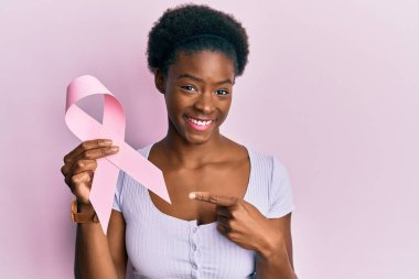 Genç Afro-Amerikalı kız pembe kanser kurdelesi tutuyor gülümsüyor. 