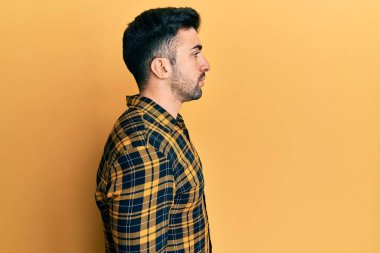 Latin kökenli genç bir adam günlük giysiler giyiyor, rahat bir görünüm takınıyor, doğal bir yüz ifadesi ve kendinden emin bir gülümsemeyle poz veriyor.. 