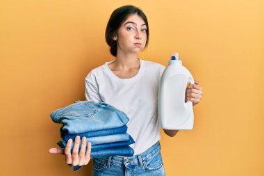 Çamaşır yıkayan, elinde deterjan şişesi olan beyaz bir kadın ve komik suratlı, katlanmış bir kot pantolon. Ağzı havayla şişer, havayı yakalar.. 