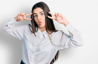 Genç esmer ergen barış jesti yapıyor. Gözleri kapalı, gözleri kısık, deli ve komik bakışlar atıyor.. 