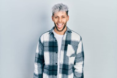 Modern boyalı saçlı, sıradan tişörtlü, komik bir ifadeyle dilini dışarı çıkaran genç İspanyol bir adam. duygu kavramı. 