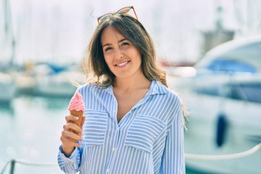 Genç İspanyol kadın gülümseyerek limanda dondurma yiyor..