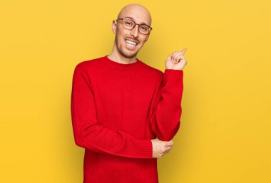 Sakallı, sıradan giyinmiş, gözlüklü, mutlu gülümseyen, eli ve parmağı yanda olan kel bir adam. 