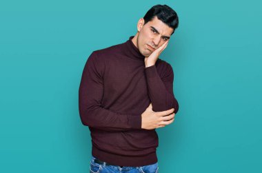 Balıkçı yaka kazak giyen yakışıklı adam kollarını kavuşturup depresyondan sıkılmış ve yorgun görünüyor.. 