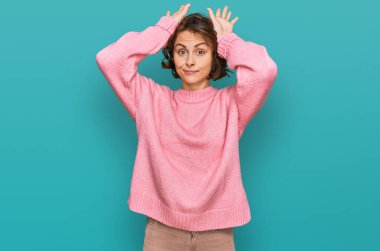 Günlük kıyafetler giyen, tavşan kulağı yapan, avuçlarıyla alaycı ve şüpheci görünen genç İspanyol kadın. Paskalya tavşanı konsepti. 