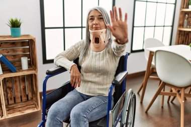 Orta yaşlı, gri saçlı, tasması açık, tekerlekli sandalyede oturan, ciddi ve kendinden emin ifadesiyle dur işareti yapan, savunma jesti yapan bir kadın. 