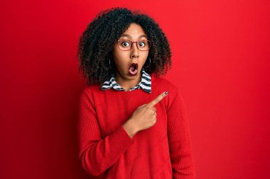 Afro saçlı, süveter giyen ve gözlüklü güzel afro-amerikalı kadın parmağını yana çevirerek şaşırdı, ağzı açık hayret içinde kaldı.. 
