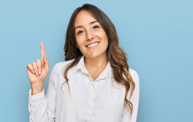 Genç esmer kadın gündelik kıyafetler giyip bir numarayı gösterip işaret ederken kendinden emin ve mutlu bir şekilde gülümsüyor.. 
