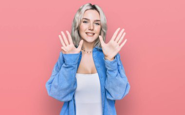 Gündelik kıyafetler giyen genç sarışın kız dokuz numarayı gösterip işaret ederken kendinden emin ve mutlu bir şekilde gülümsüyor.. 