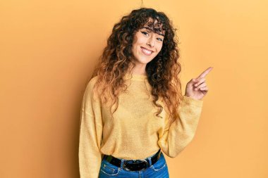 Yüzünde kocaman bir gülümseme olan, gündelik kıyafetler giyen genç İspanyol kız, kameraya el ve parmak ile bakıyor.. 