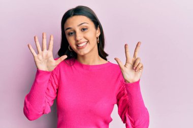 Genç İspanyol kadın gündelik kıyafetler giyer ve sekiz numaralı parmaklarıyla gülümseyerek mutlu ve kendinden emin bir şekilde işaret eder.. 