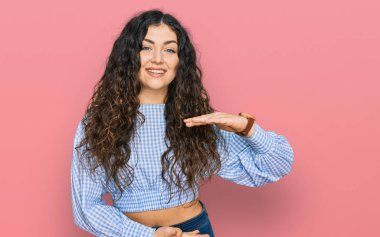 Latin kökenli genç bir kız, sıradan kıyafetler giyiyor. Elleriyle işaret ediyor. Ölçü sembolü. Kameraya bakıp gülümsüyor. ölçüm kavramı. 