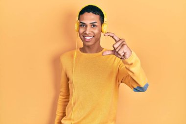 Genç Afro-Amerikalı adam kulaklık takarak müzik dinliyor. Gülümsüyor ve el hareketleriyle el hareketi yapıyor. Parmaklarıyla işaret yapıyor ve kameraya bakıyor. ölçüm kavramı. 