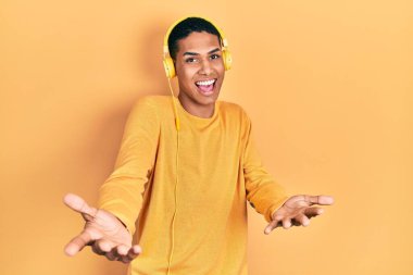 Genç Afrikalı Amerikalı adam kulaklık takarak müzik dinliyor. Kollarını açıp gülümsüyor. Dostça karşılama, olumlu ve kendinden emin selamlar. 