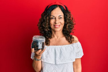 Orta yaşlı, elinde kahve çekirdekleri olan İspanyol bir kadın pozitif ve mutlu görünüyor ve gülümseyerek dişlerini gösteriyor. 