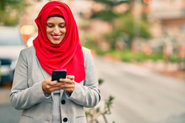 Şehirde akıllı telefon kullanan tesettürlü genç Arap iş kadını..