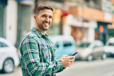 Beyaz adam şehirde akıllı telefon kullanarak mutlu bir şekilde gülümsüyor..
