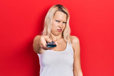 Televizyonun uzaktan kumandalı kumandalı, kafası karışık ve kafası karışık güzel beyaz bir kadın. şüphe kavramı. 