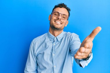 Gündelik kıyafetler ve gözlük takan genç İspanyol adam dostça bir selamlama ve hoş geldin hediyesi olarak el sıkışmayı sunuyor. başarılı iş. 