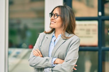 Kollarını kavuşturup şehirde mutlu bir şekilde gülümseyen genç İspanyol iş kadını.