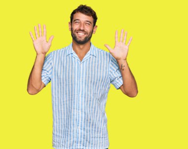Sakallı yakışıklı genç adam, günlük temiz gömleğini giyiyor ve parmaklarını on numaraya gösteriyor. Kendinden emin ve mutlu gülümsüyor.. 