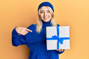 Genç beyaz kadın elinde hediyeyle mutlu bir şekilde gülümsüyor. 