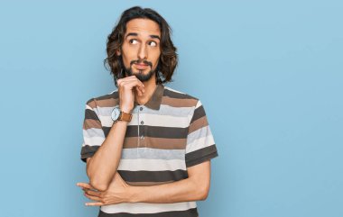 Elleri çenesinde gündelik giysiler içinde soru soran genç İspanyol bir adam, düşünceli bir ifade. Gülümseyen ve düşünceli bir yüz. şüphe kavramı. 