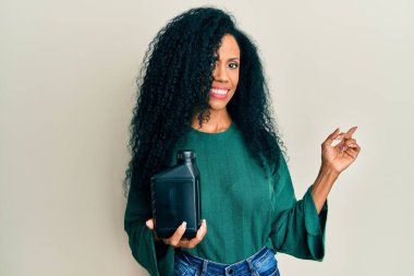 Orta yaşlı Afro-Amerikalı kadın, elinde yağ şişesi, gülümsüyor. 