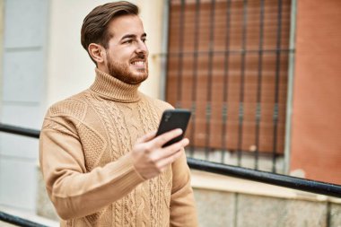 Beyaz adam şehirde akıllı telefon kullanarak mutlu bir şekilde gülümsüyor..