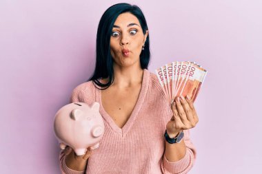 Elinde Norveç kronu banknotları ve domuz kumbarası olan beyaz bir kadın balık suratlı, şaşı, çılgın ve komik gözlerle bakıyor.. 