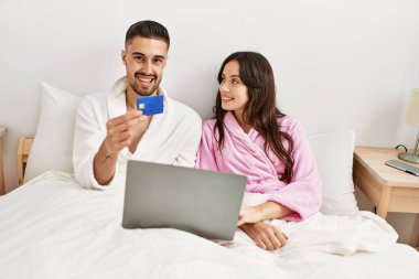 Evde yatan genç İspanyol çift dizüstü bilgisayar ve kredi kartı kullanıyor..