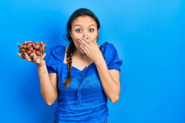 Genç İspanyol kız elinde bir kase kestaneyle ağzını eliyle kapatıyor, şokta ve hata yapmaktan korkuyor. şaşırmış ifade 