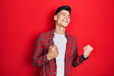 Gündelik kıyafetler giyen genç İspanyol adam başarı için heyecanlı kolları havada ve gözleri kapalı zaferi kutlarken gülümsüyor. Kazanan konsept. 