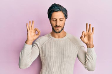 Günlük kazak giyen genç İspanyol adam rahatla ve gülümse gözleri kapalı parmaklarıyla meditasyon hareketi yapıyor. yoga konsepti. 
